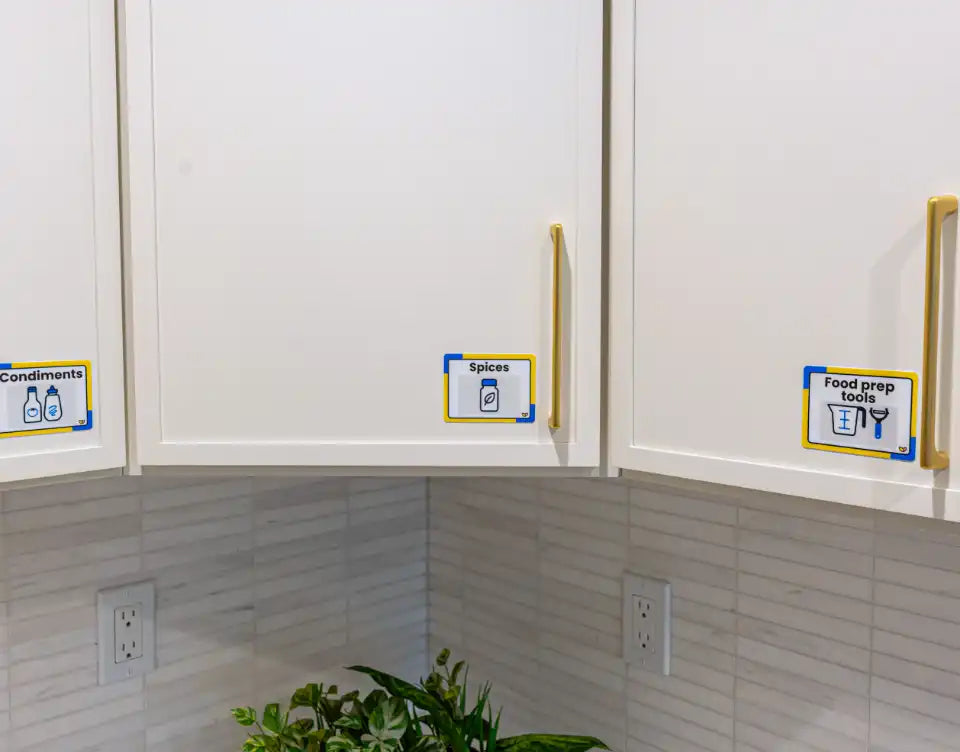 A Mugs label and familiar mug photograph mark the kitchen cupboard where the cups are stored, supporting visual aids for memory loss.